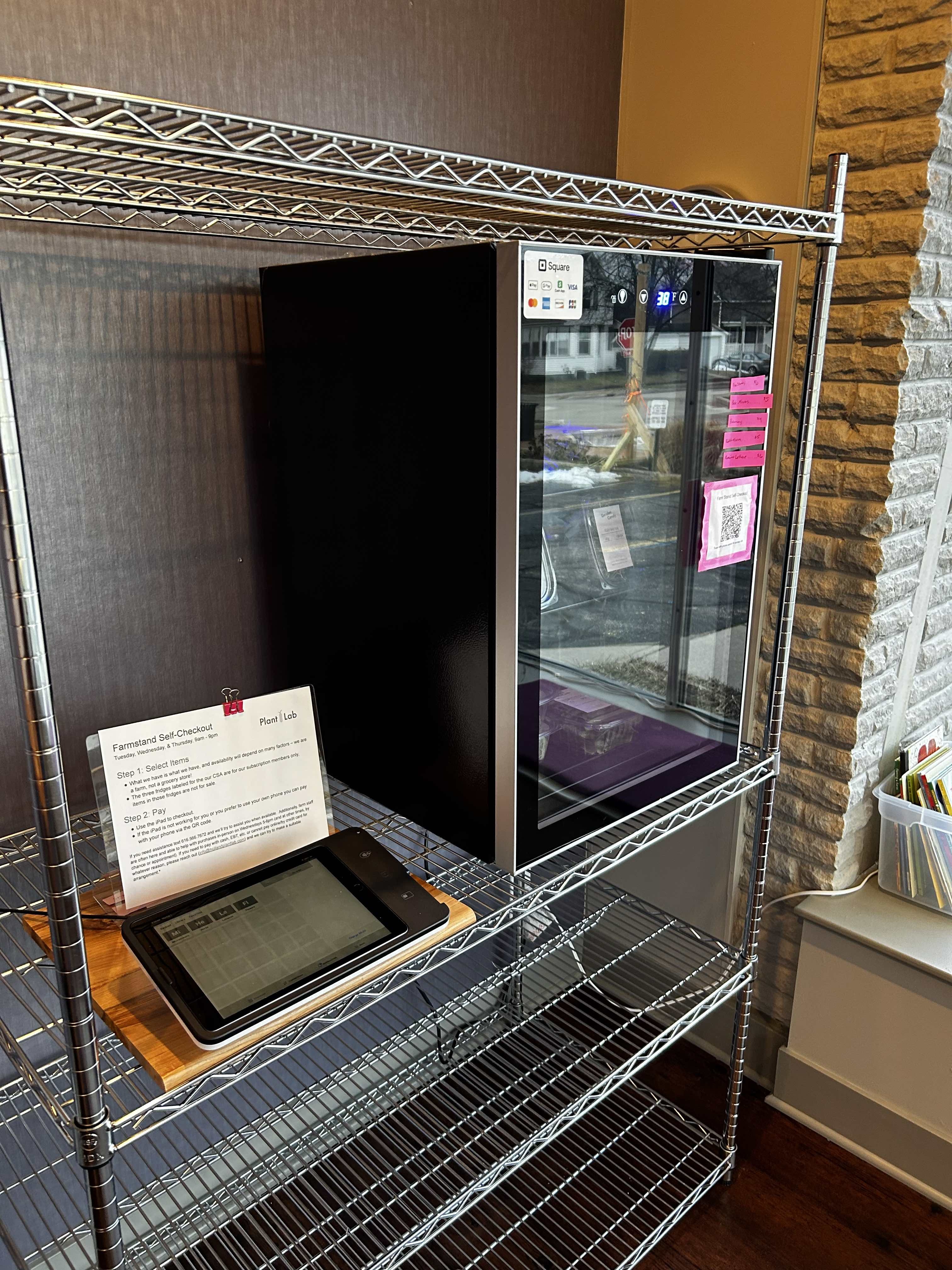 an ipad on a shelf next to a small fridge full of packaged salad greens